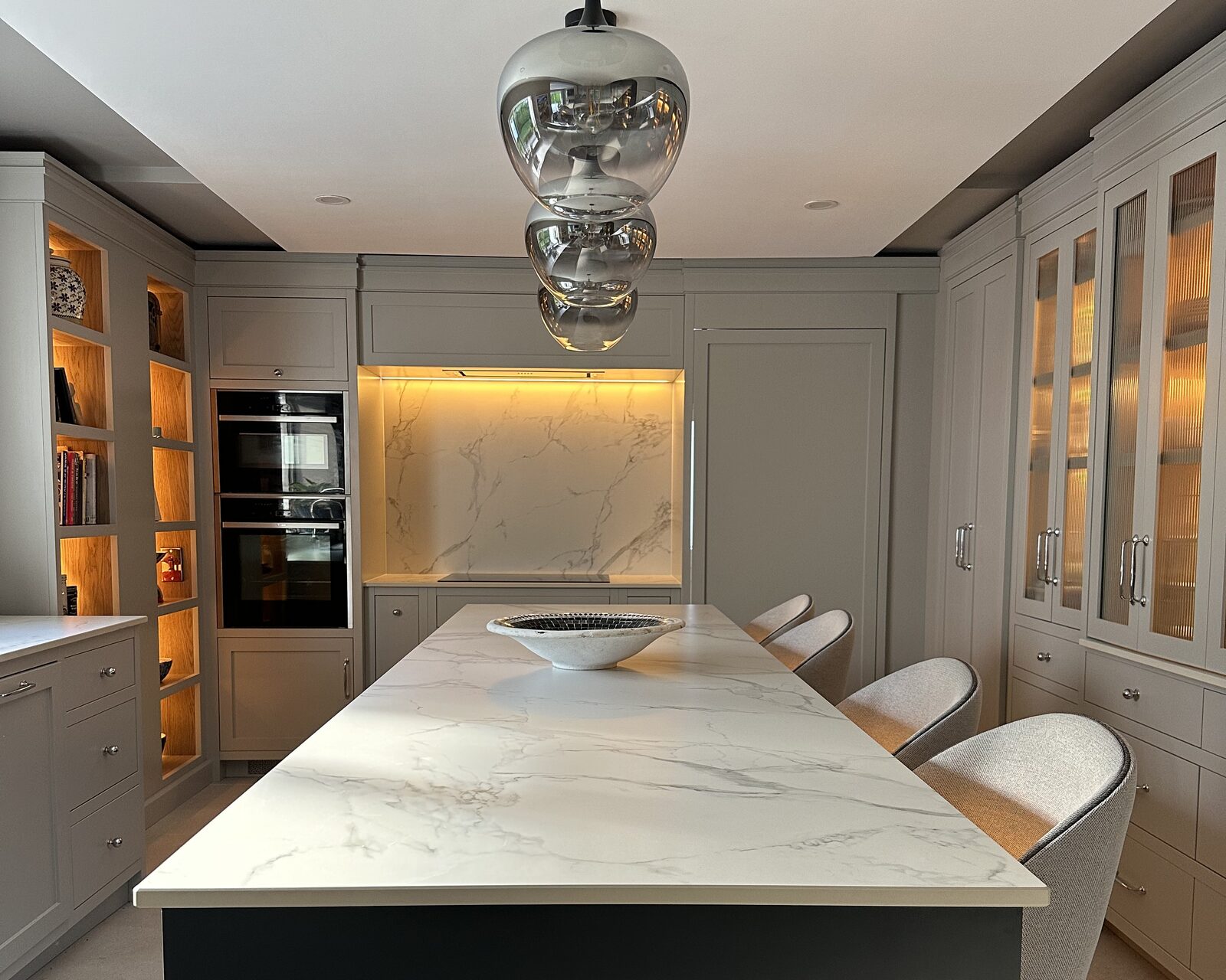 A bespoke painted kitchen with a dark island, marble-effect worktop and glass-fronted cabinets by Willow Design